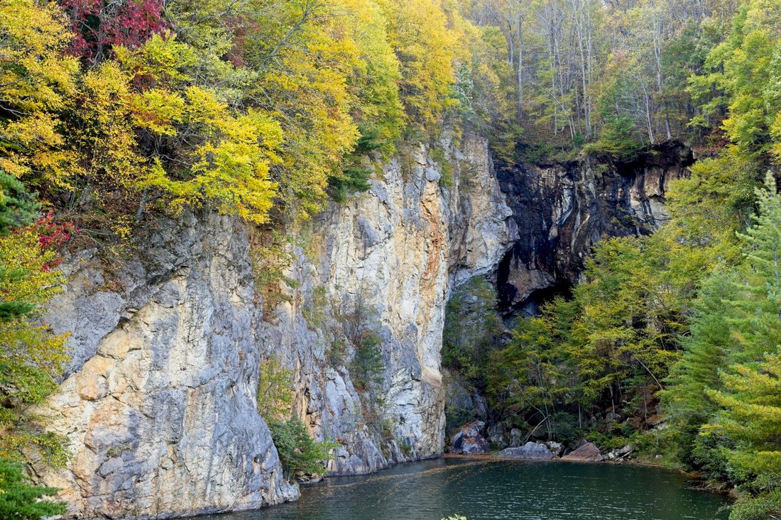 Pale rock cliff above a still pond ringed with red and gold autumn foliage — Emerald Village, Blue Ridge Parkway