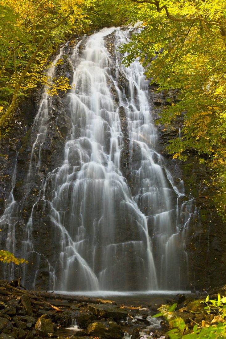 Veil-like waterfall cascading down mossy black rock through soft yellow forest light — Crabtree Falls, Blue Ridge Parkway